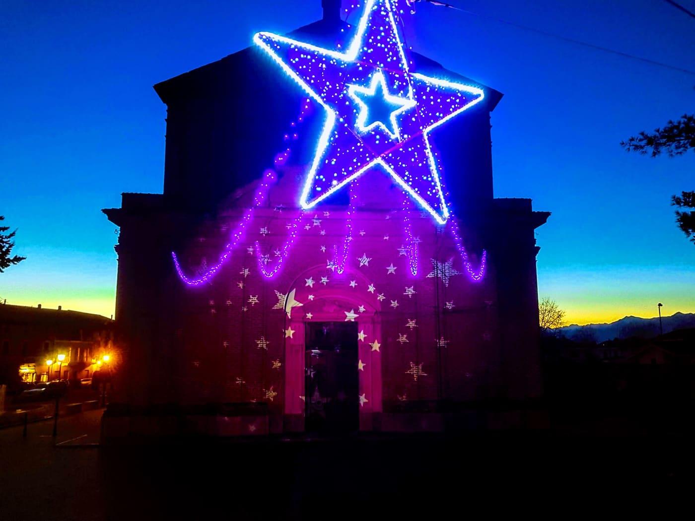 Grande stella luminosa sulla facciata di una chiesa, contro il cielo del tramonto
