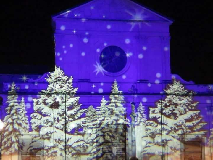 Proiezione di abeti innevati sulla facciata di una chiesa illuminata di blu