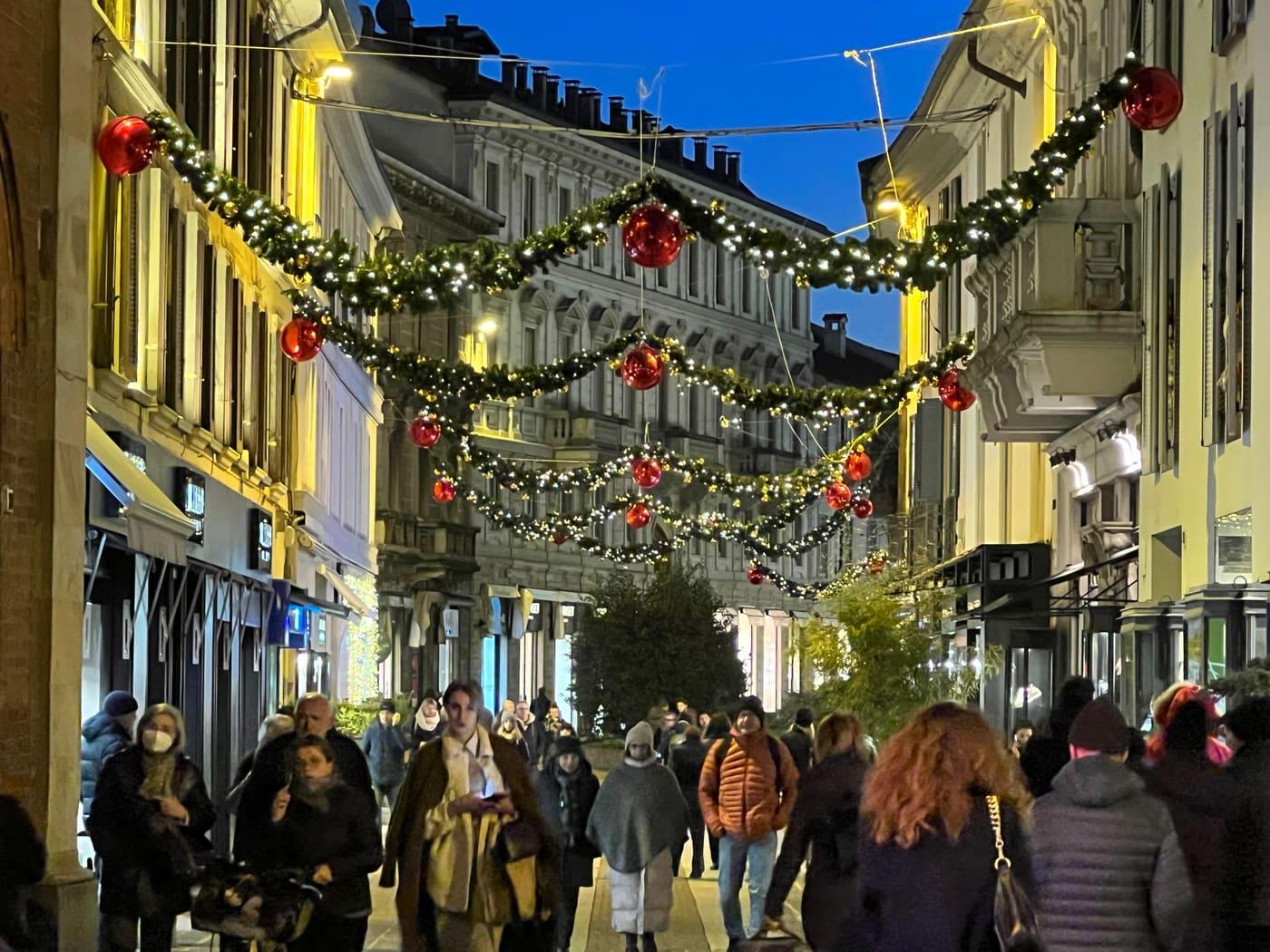 Via del centro con festoni verdi e sfere rosse sospesi, negozi illuminati
